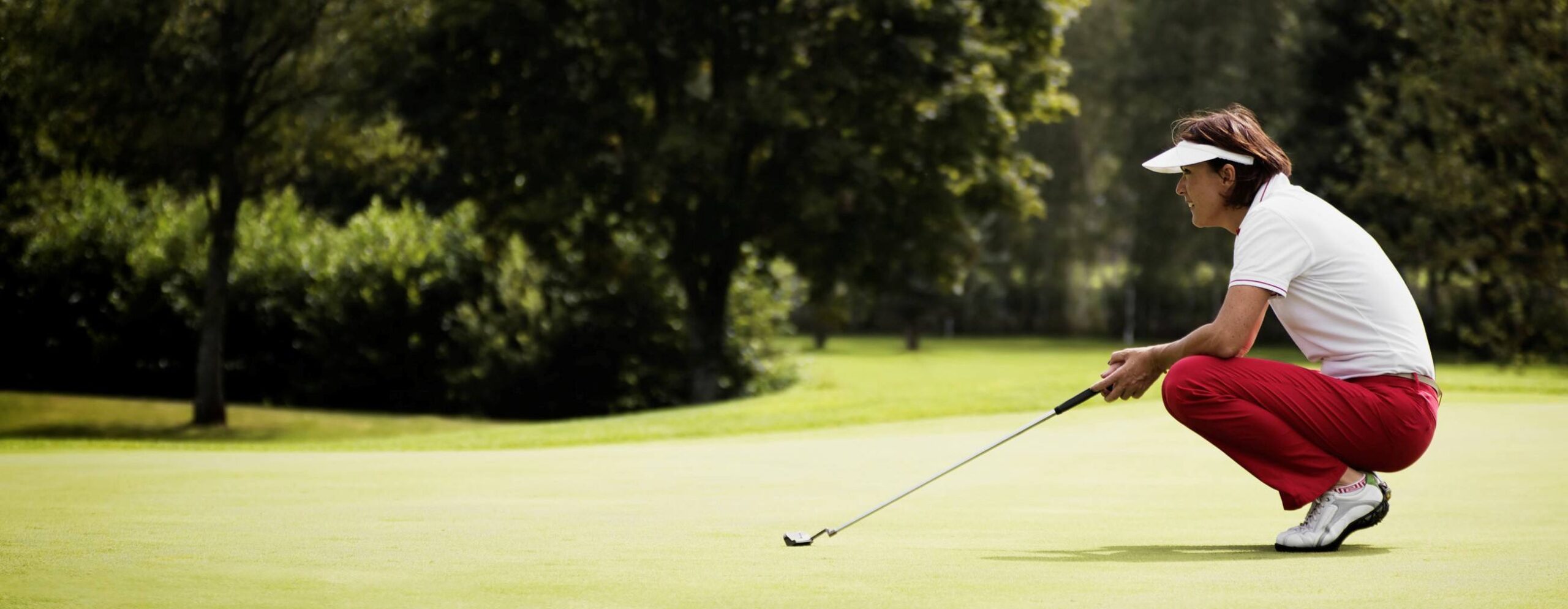 Female golf player with putter squatting to study the green at golf course.